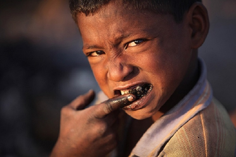 A homeless boy cleans his teeth with coal